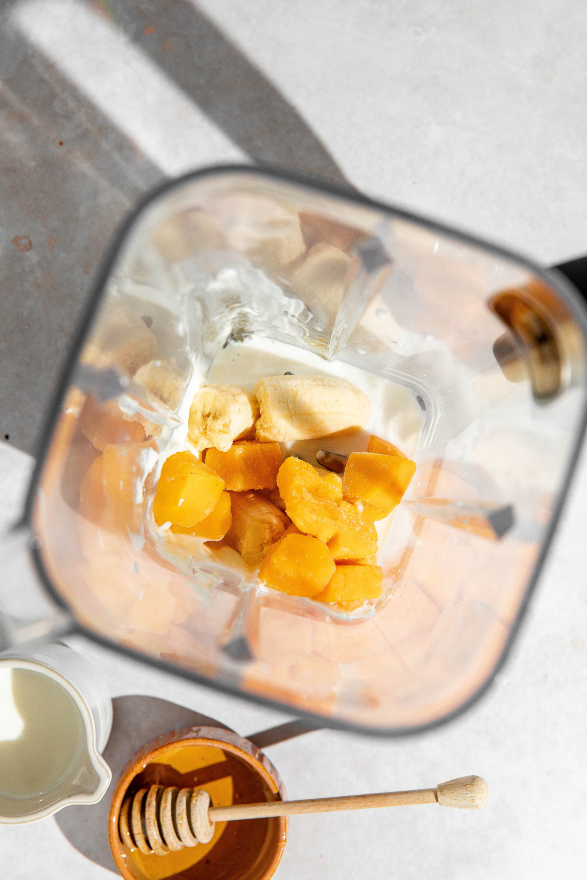 Frozen mango, banana, coconut milk and honey in a blender jar.