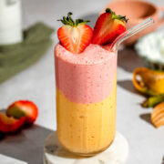 A layered strawberry mango smoothie garnished with fresh strawberries.