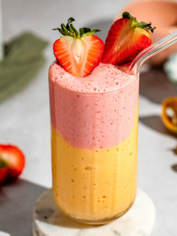 A layered strawberry mango smoothie garnished with fresh strawberries.