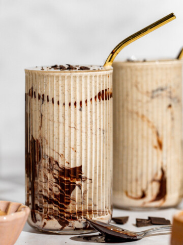 Two glasses of chocolate peanut butter smoothie sitting on a white countertop.