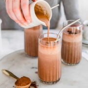 A mocha smoothie being poured from a jug into a tall glass.