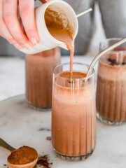 A mocha smoothie being poured from a jug into a tall glass.