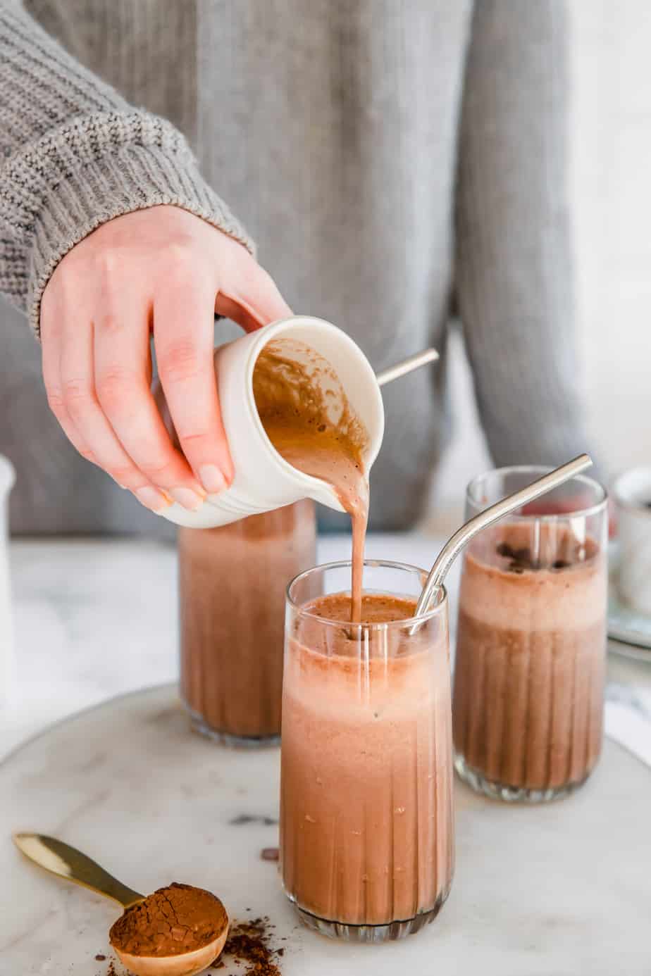 A mocha smoothie being poured from a small pitcher into a tall glass. 