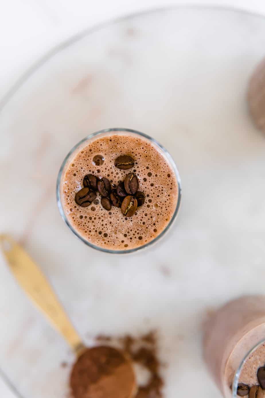 A glass of mocha smoothie garnished with coffee beans sitting on a marble tray.