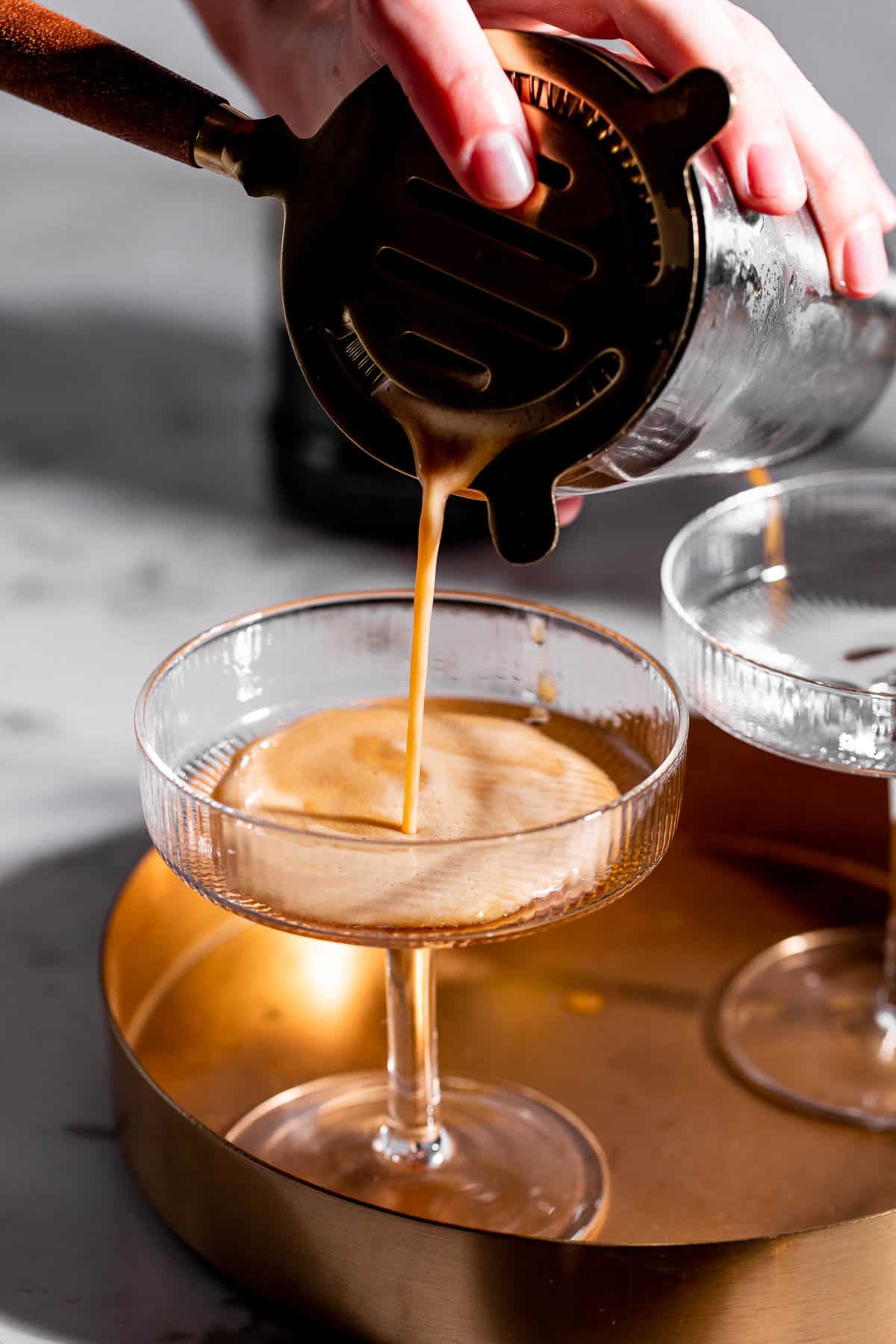 An espresso martini being poured into a martini glass.