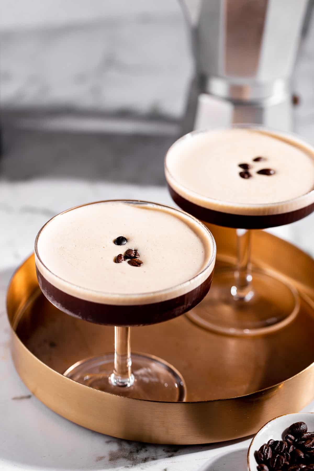 Two tequila espresso martinis on a gold tray garnished with coffee beans.