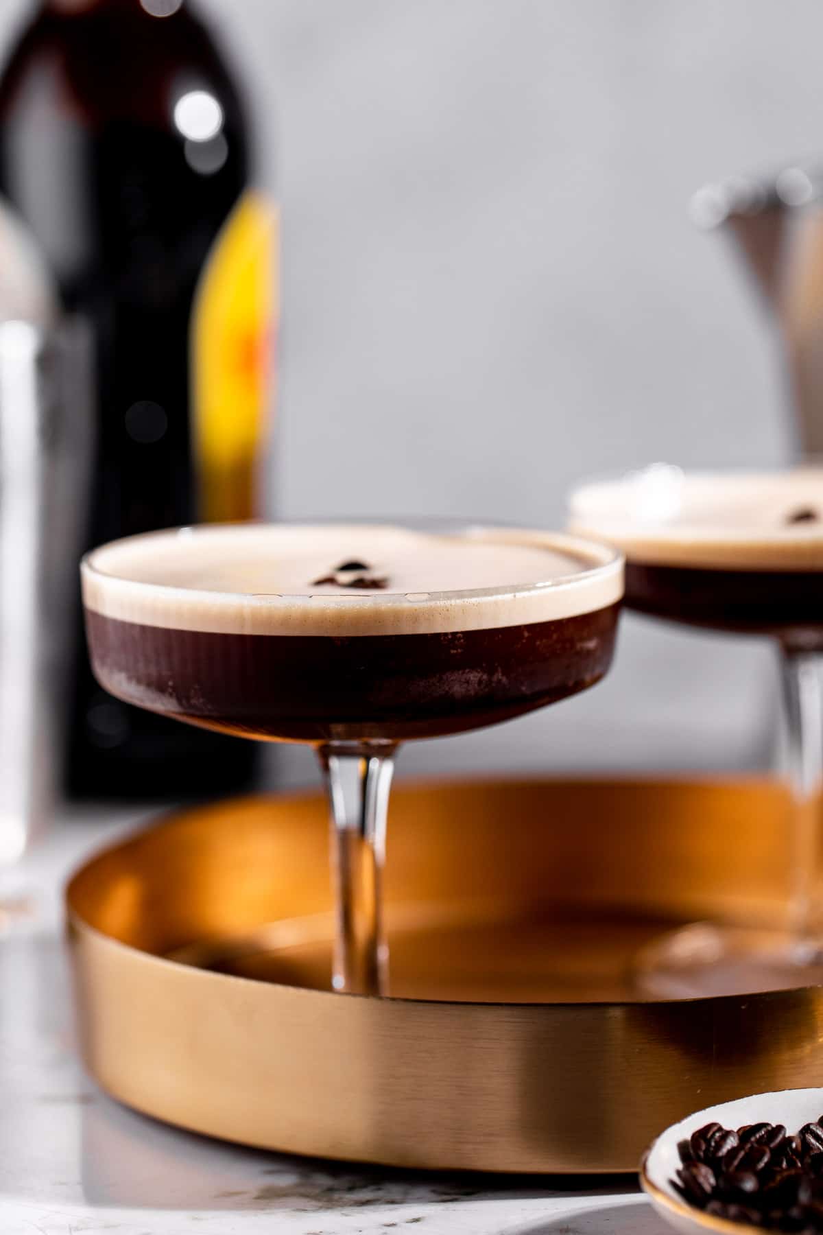 A tequila espresso martini on a gold tray garnished with coffee beans.