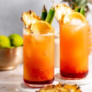 Two highball glasses filled with bay breeze cocktail and garnished with dried pineapple slices.