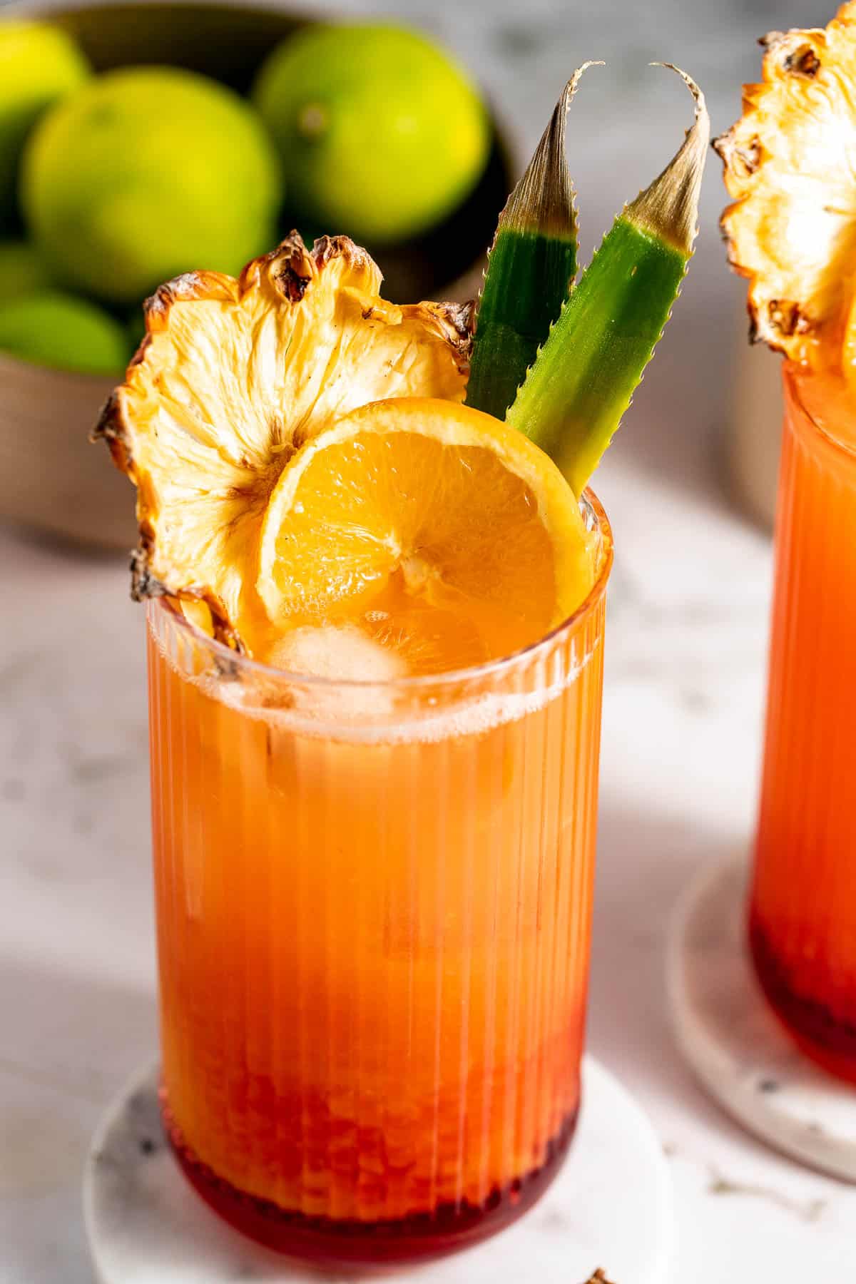 A bay breeze cocktail served in a highball glass and garnished with pineapple and orange slices.