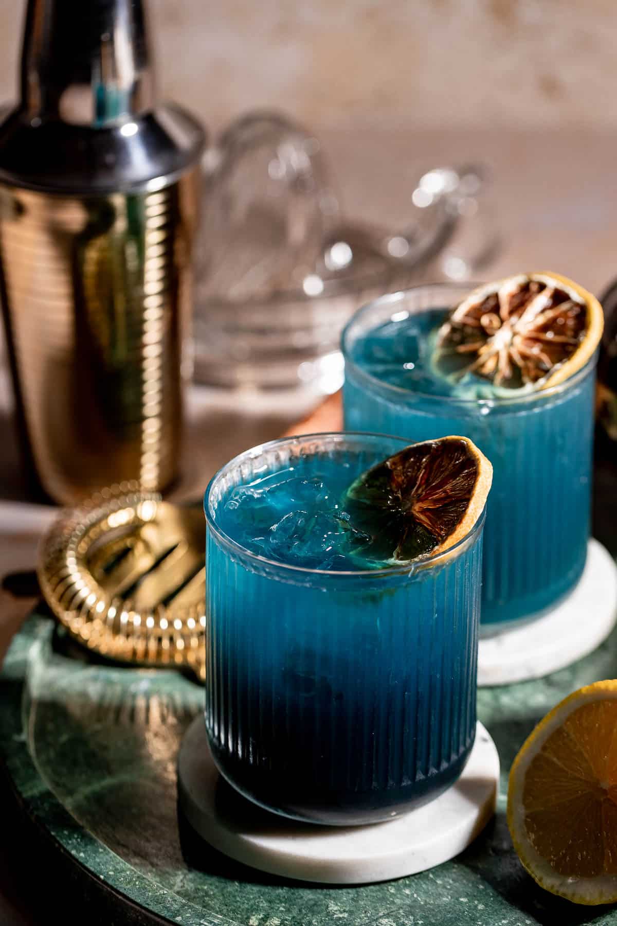 Two glasses of black opal cocktail on a green marble serving tray.