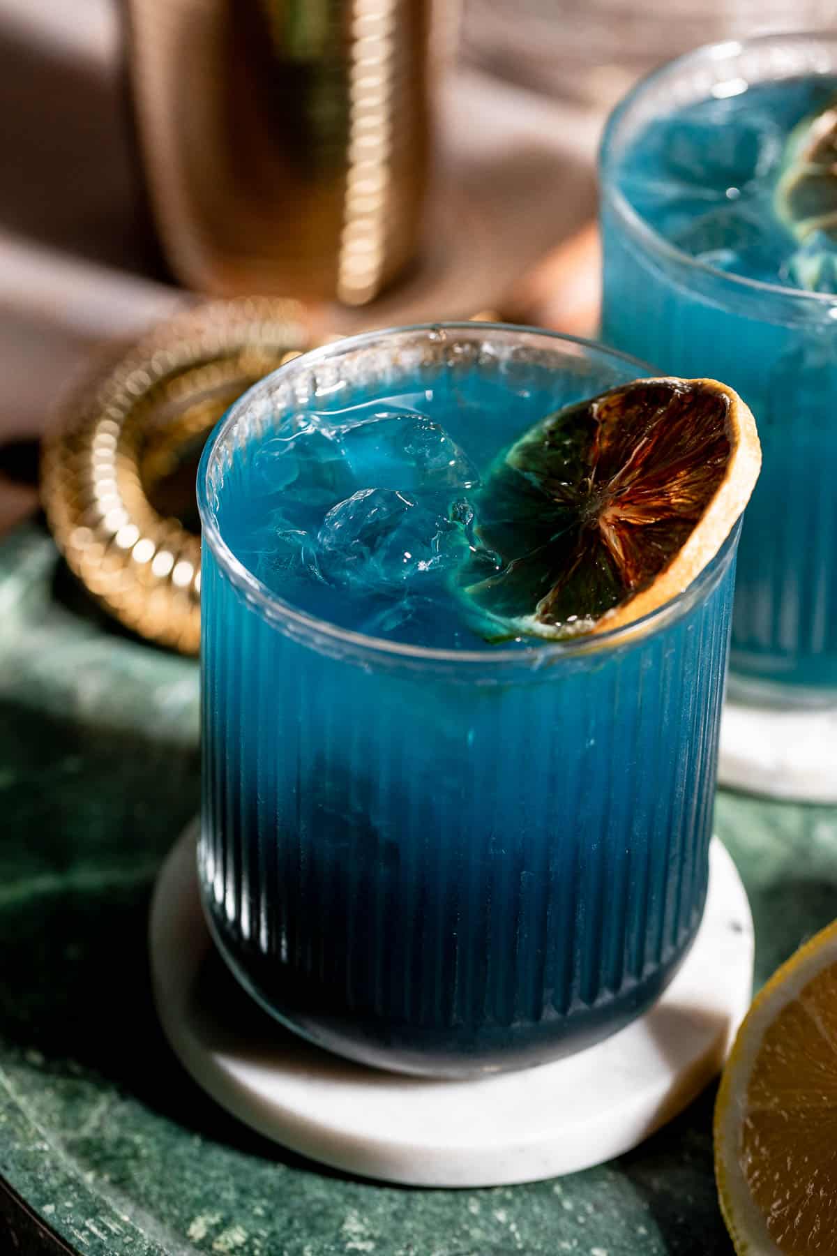 A black opal drink topped with a lemon slice sitting on a marble coaster.