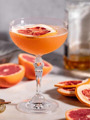 A brown derby cocktail sitting on a counter next to several grapefruit slices.