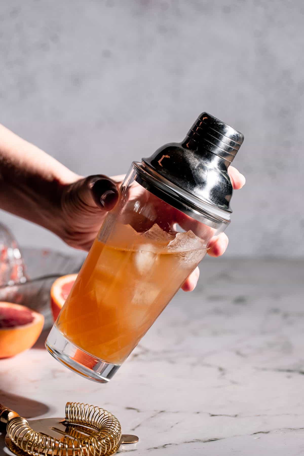 A brown derby cocktail being prepared in a glass cocktail shaker.