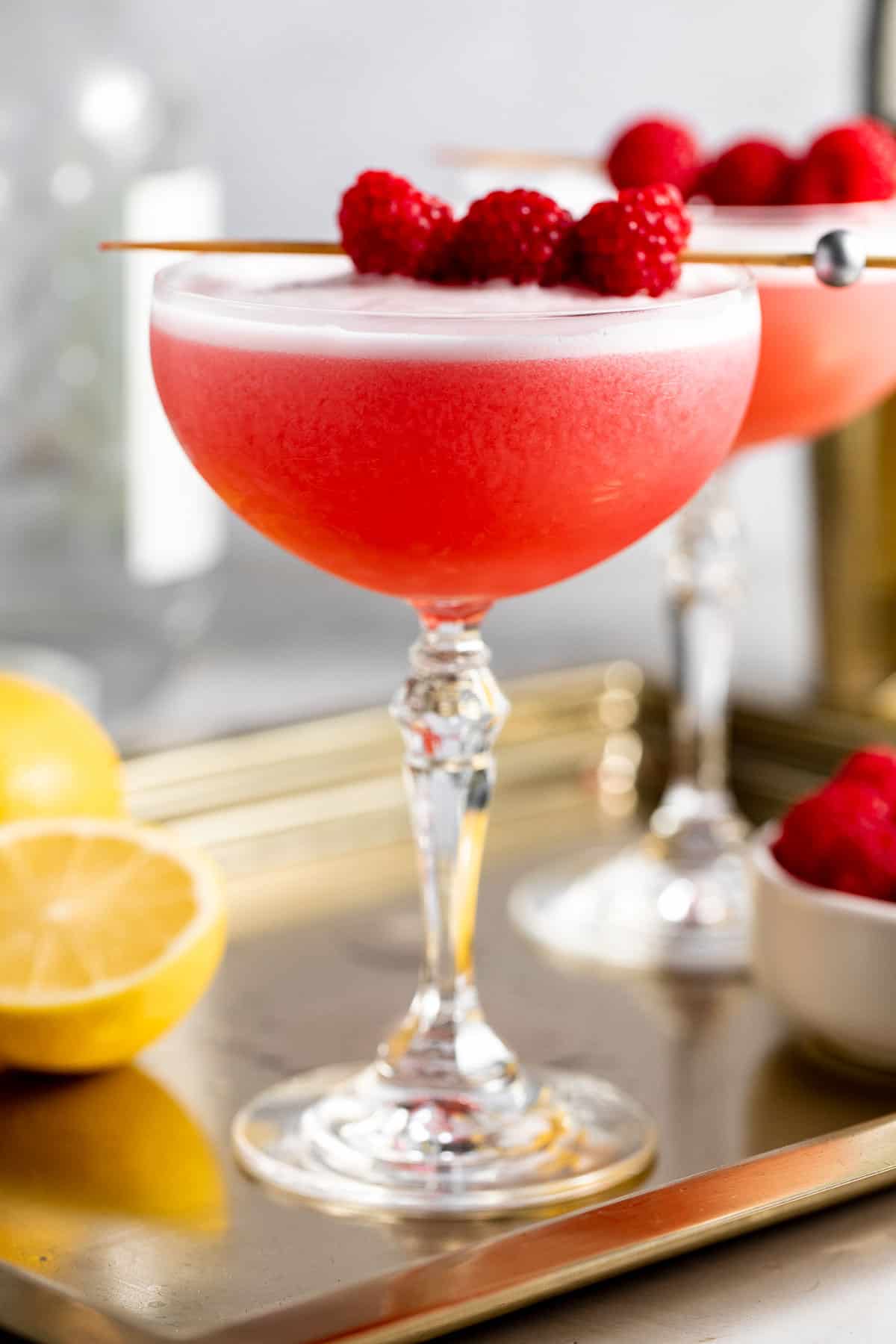 Two coupe glasses filled with clover club cocktail and topped with fresh raspberries.