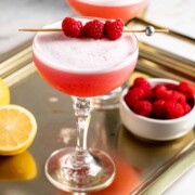 Two clover club cocktails served in coupe glasses sitting on a gold tray.