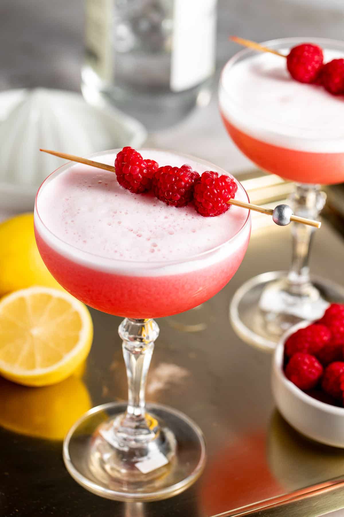 Two coupe glasses filled with colorful clover club cocktails topped with fresh raspberries.