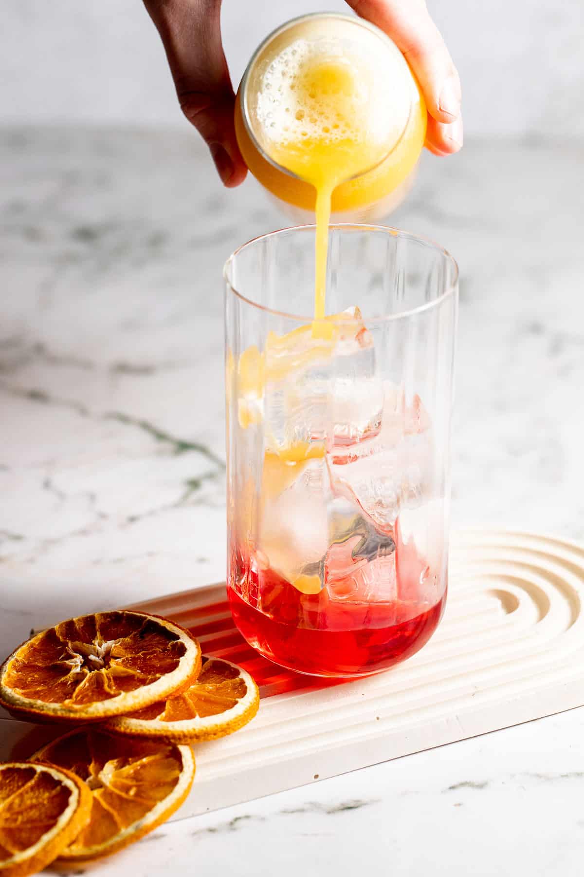 Orange juice being poured into Campari to create a Garibaldi cocktail.