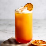 A garibaldi cocktail garnished with an orange slice on a small wooden tray.