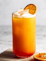 A garibaldi cocktail garnished with an orange slice on a small wooden tray.