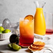A madras cocktail served in a high ball glass sitting next to a carafe of orange juice.