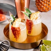 Two mezcalitas garnished with pineapple slices sitting on a gold tray.