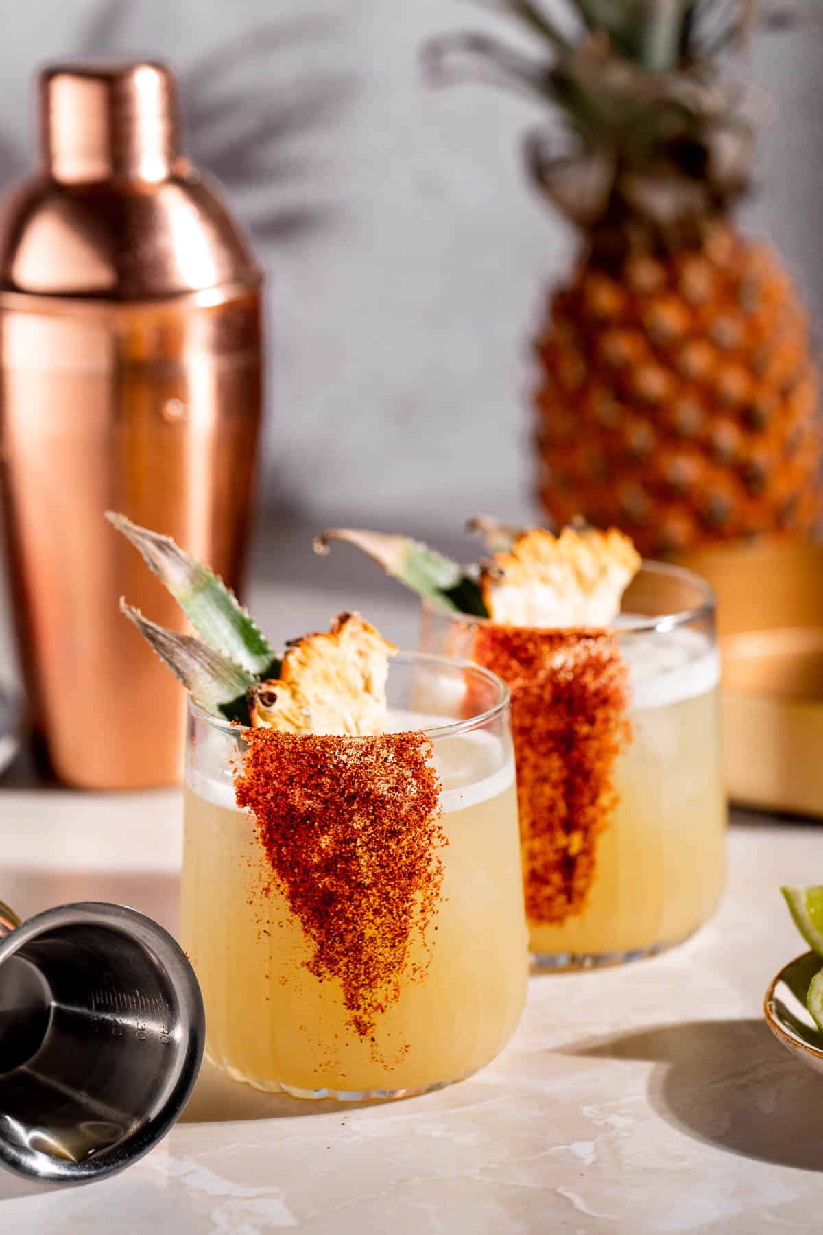 Two mezcalitas served with pineapple wedges sitting on a marble table.