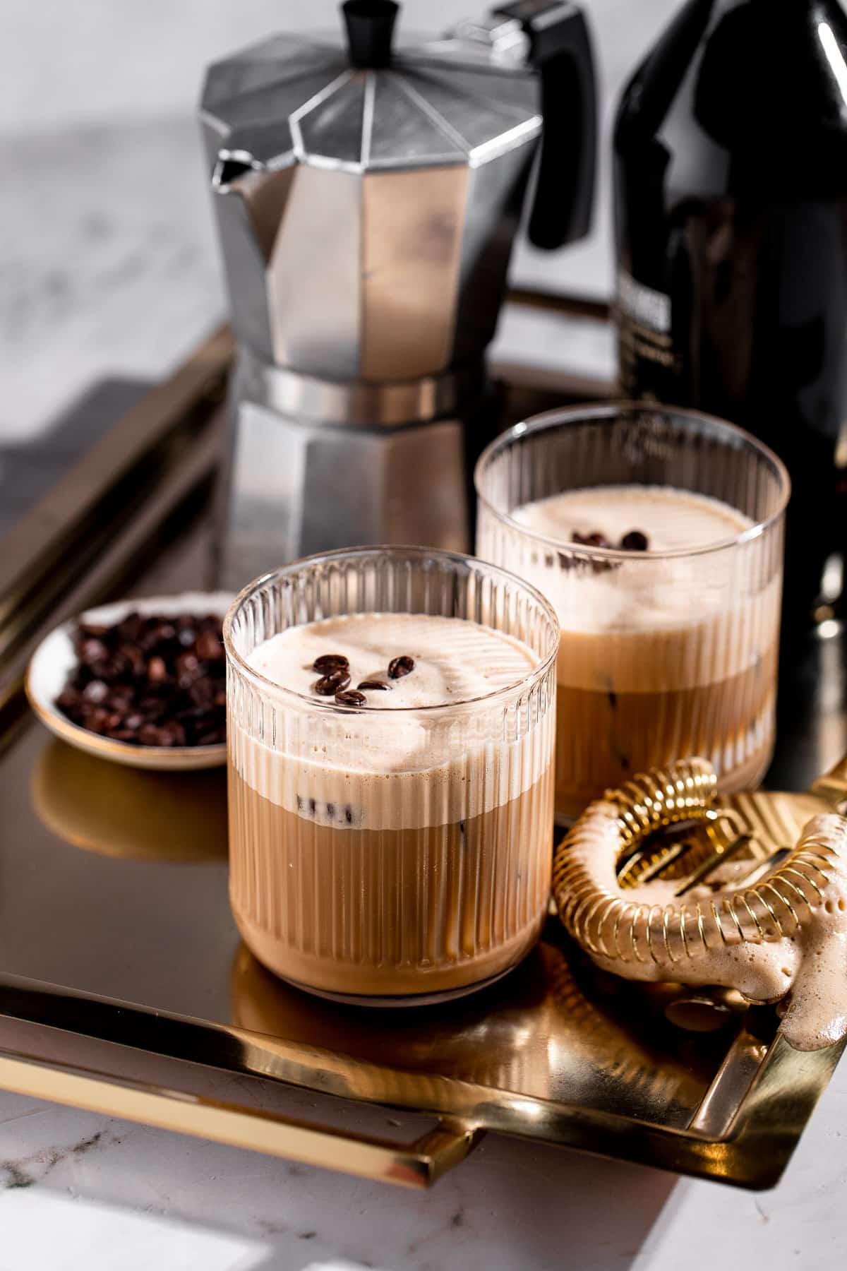 Two glasses of shaft drink sitting on a gold tray next to a coffee pot.