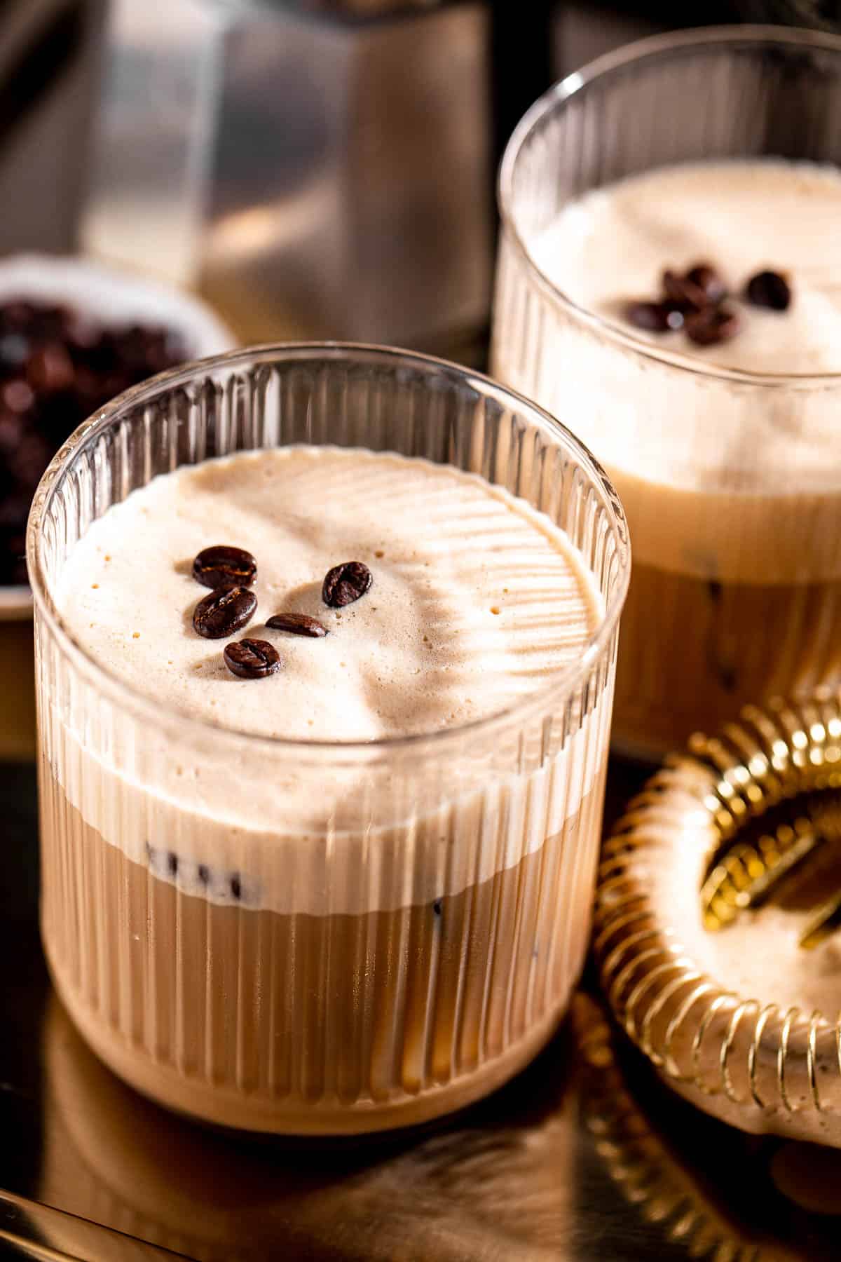 Two glasses of shaft cocktail topped with coffee beans sitting on a gold tray.