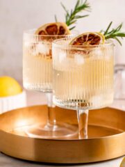 Two glasses of whiskey and tonic sitting on a gold serving tray.