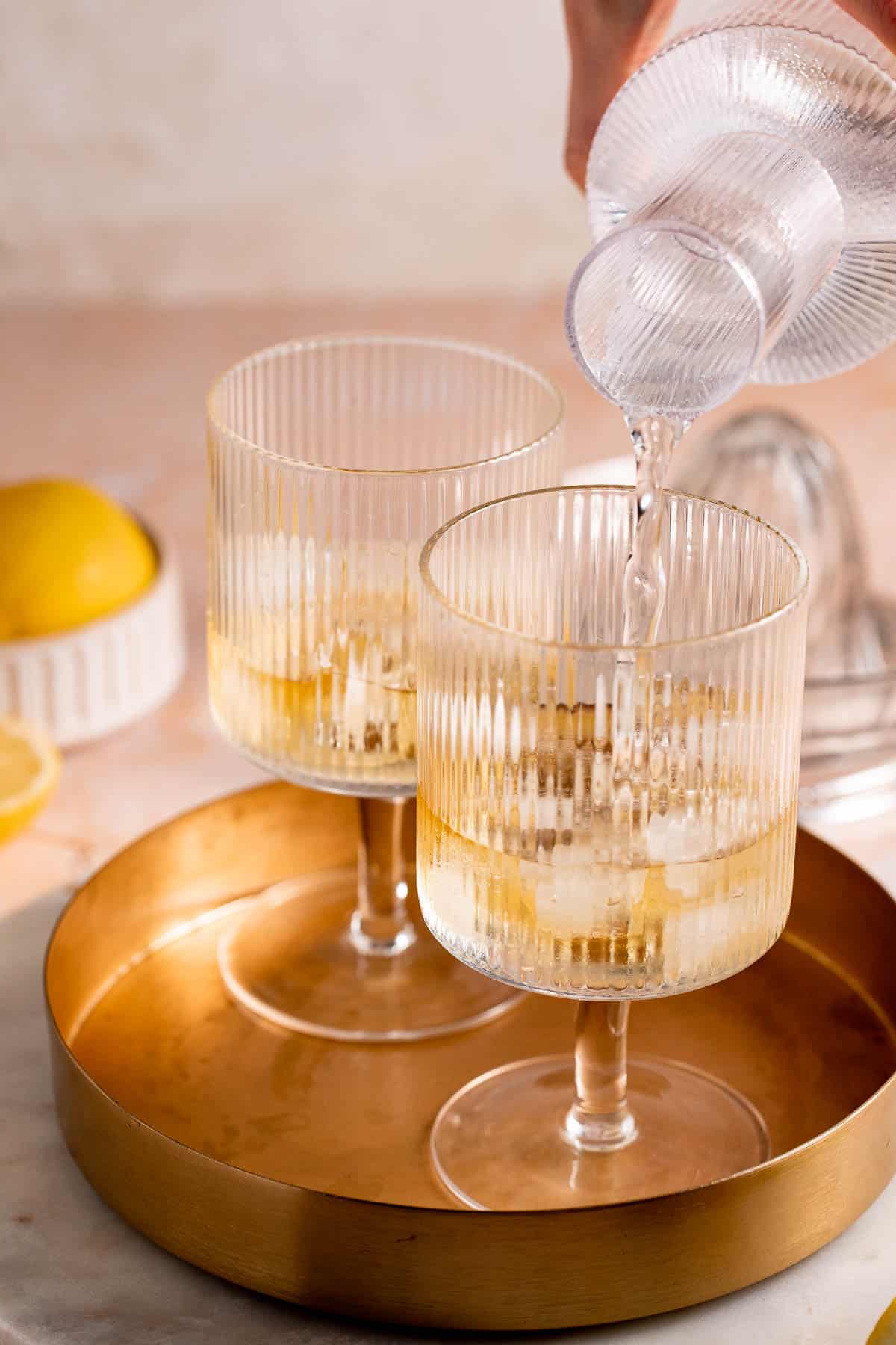 Tonic water being poured into a serving glass with ice and whiskey.