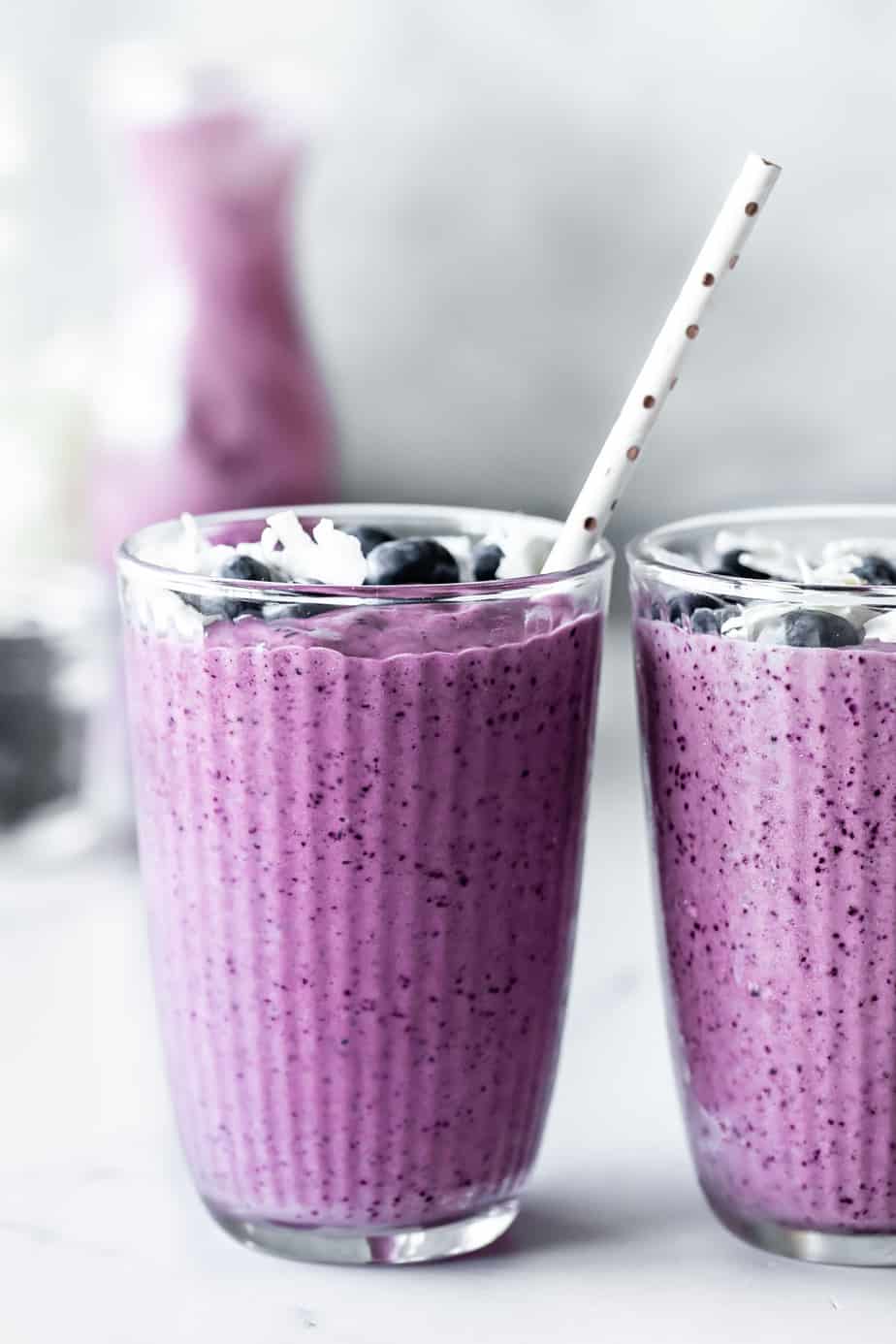 Two glasses of blueberry pineapple smoothie with a straw sticking out.