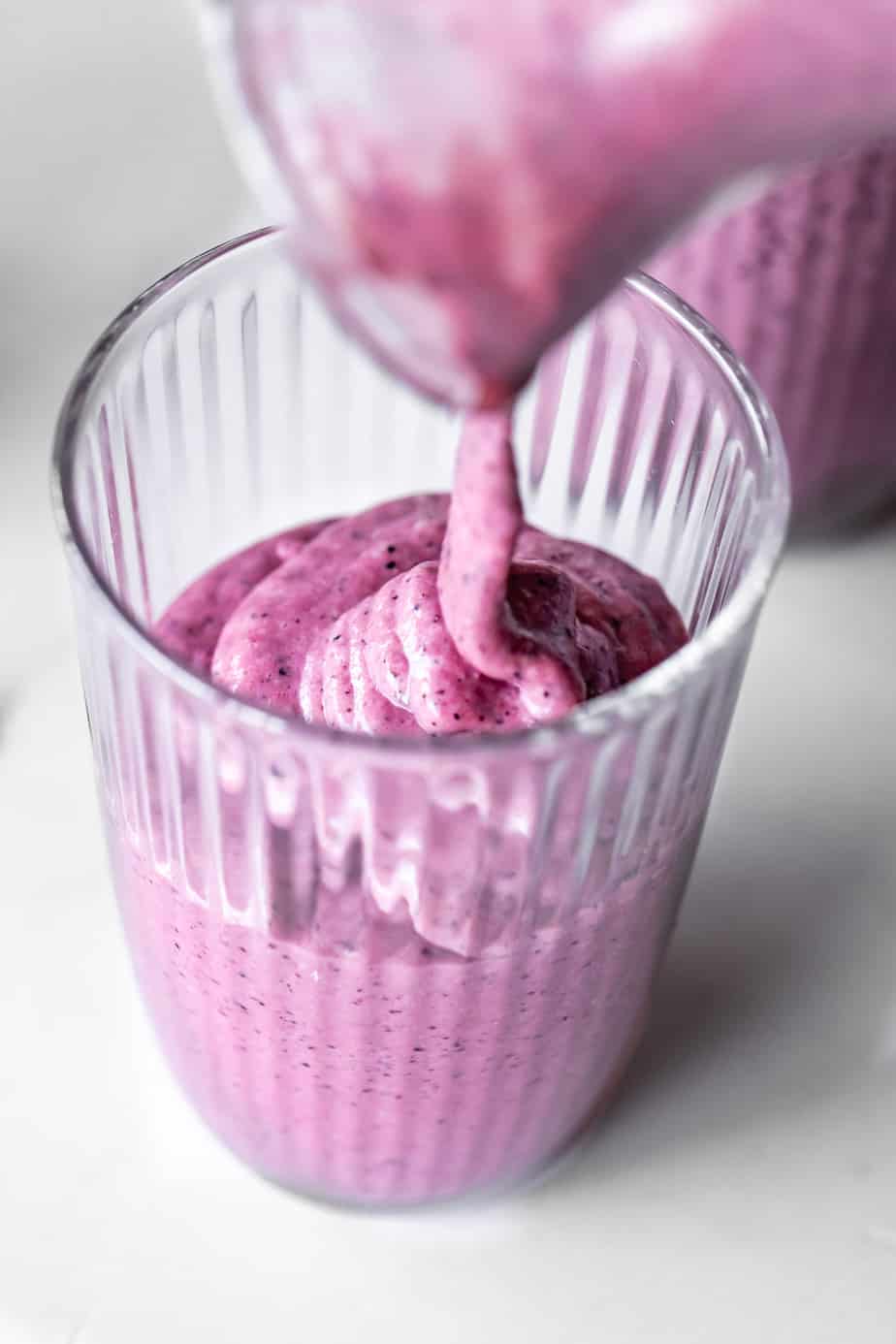 Blueberry pineapple smoothie being poured into a glass.