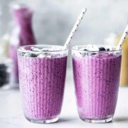 Two blueberry pineapple smoothies sitting on a countertop.