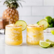 Two spicy pineapple margaritas garnished with lime wheels.