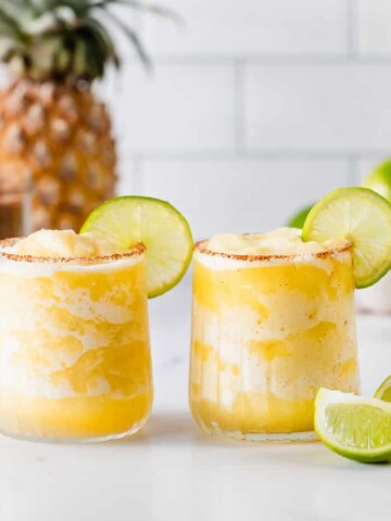 Two spicy pineapple margaritas garnished with lime wheels.