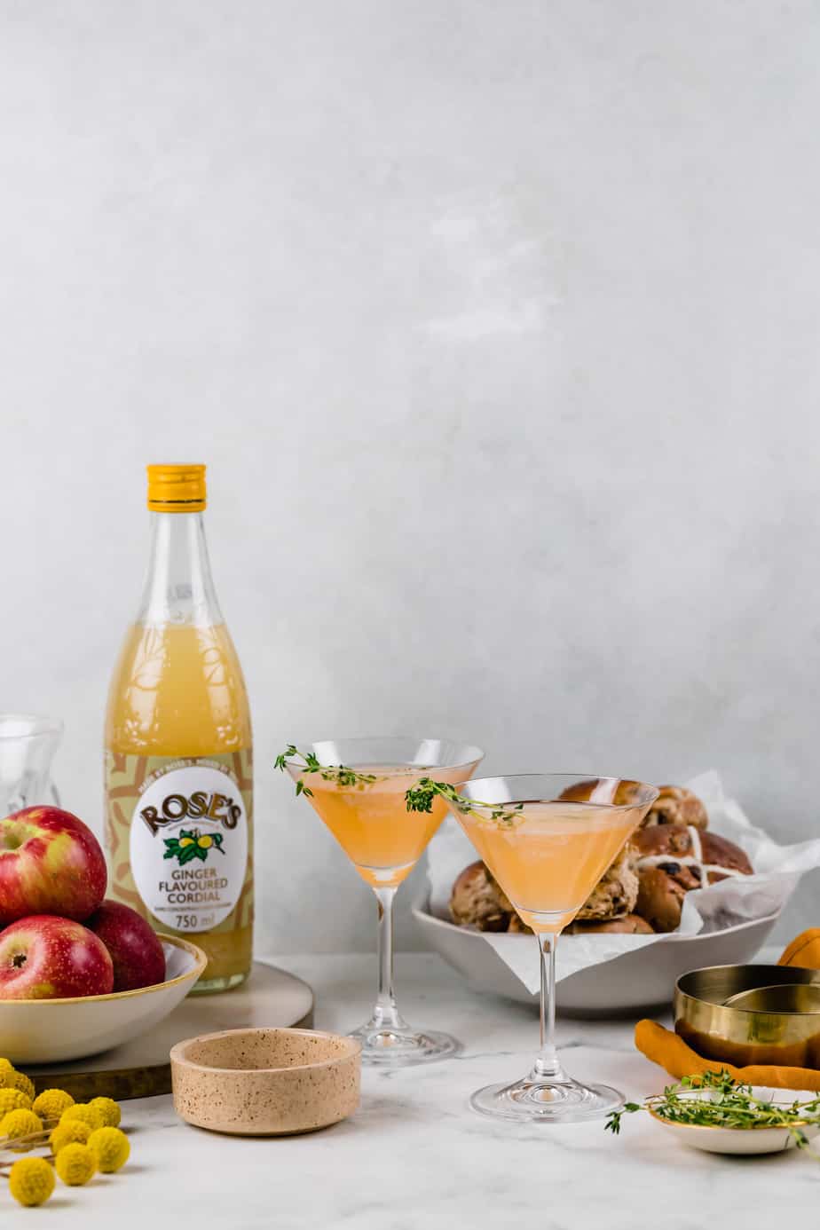 Two spiced apple cider cocktails in martini glasses sitting on a marble countertop.