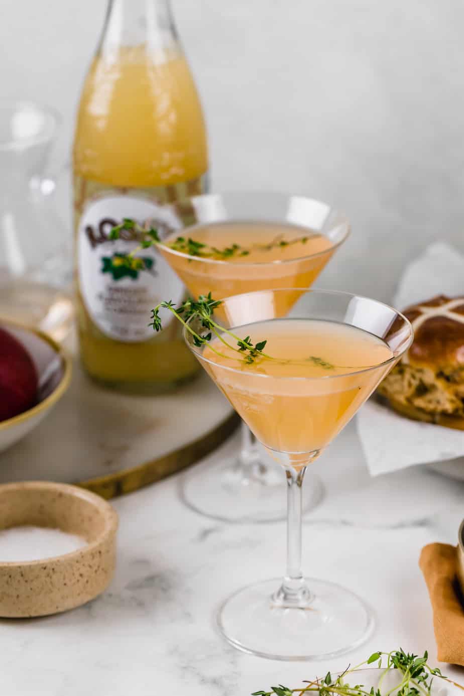 Two martini glasses filled with spiced apple cider cocktail and garnished with fresh thyme.