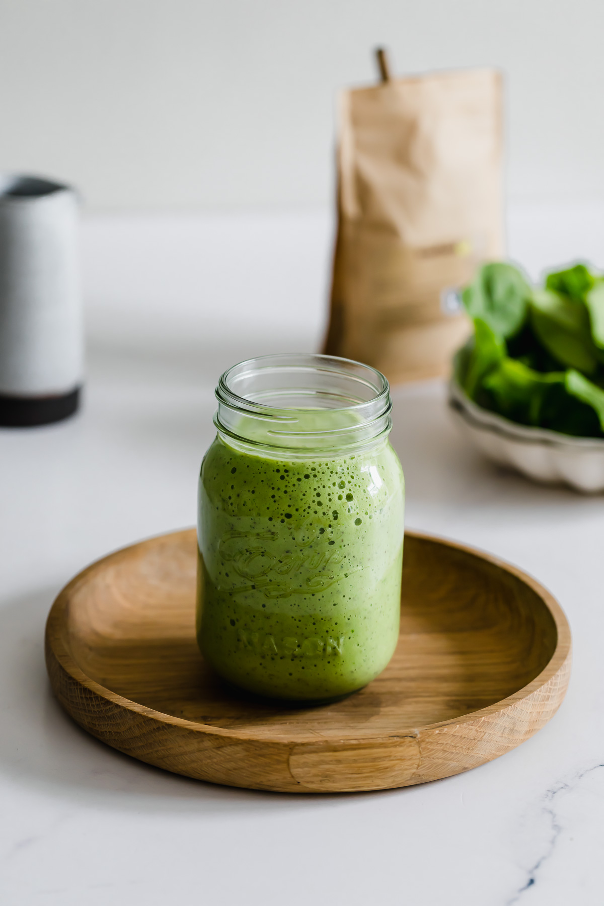 A spinach and pineapple smoothie served in a mason jar sitting on a wood tray.