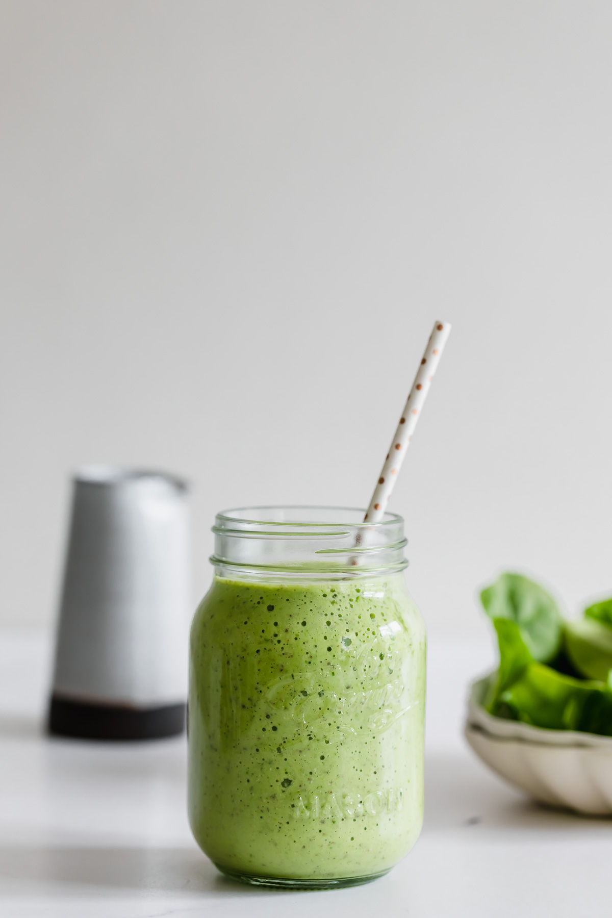 A spinach and pineapple smoothie served in a mason jar with a straw.