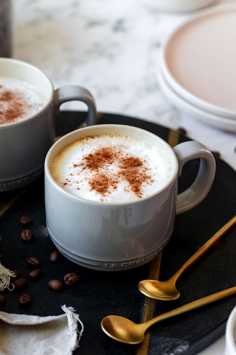 A coffee mug filled with oat milk latte topped with ground cinnamon sitting on a serving tray.