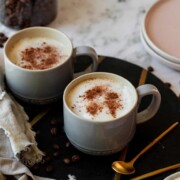 Two coffee mugs filled with oat milk lattes topped with ground cinnamon.