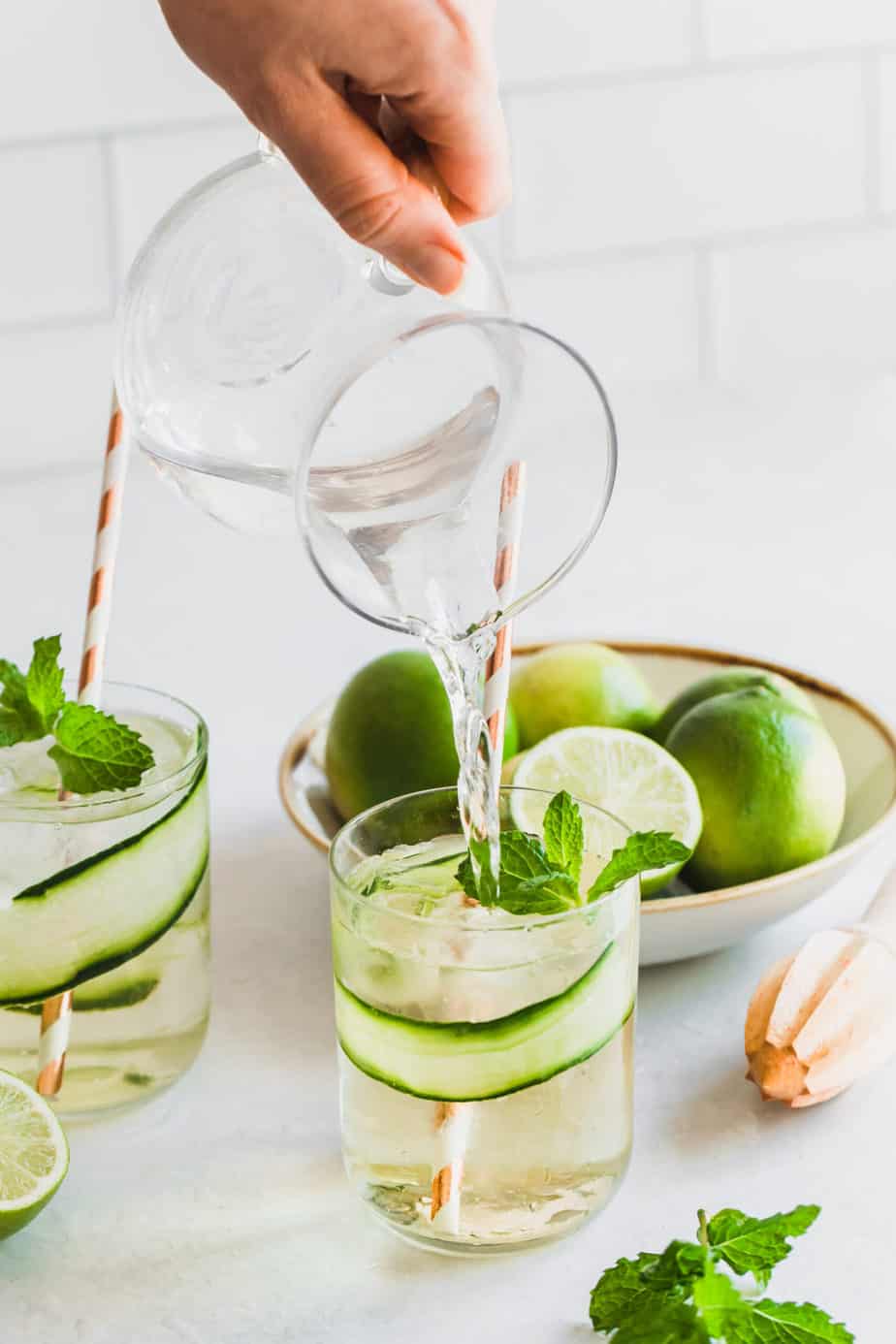 Tonic water being poured into two glasses of cucumber gin and tonic.