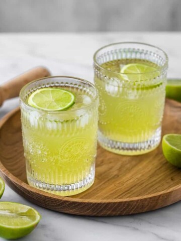 Two glasses of Tokyo Tea sitting on a round wooden tray.