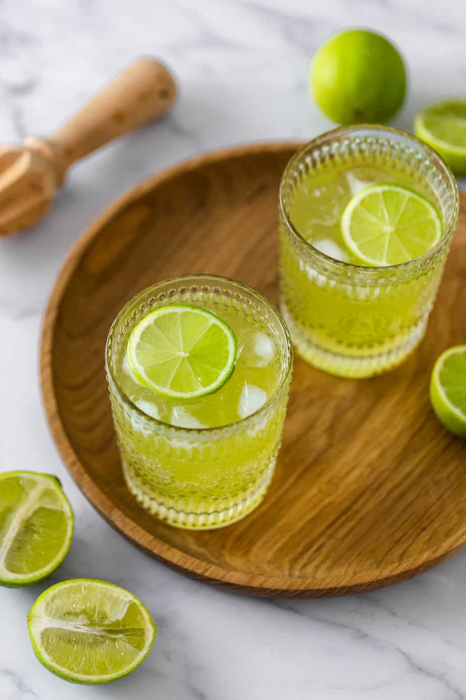 The glasses of Tokyo iced tea sitting on a wooden tray surrounded by lime wedges.