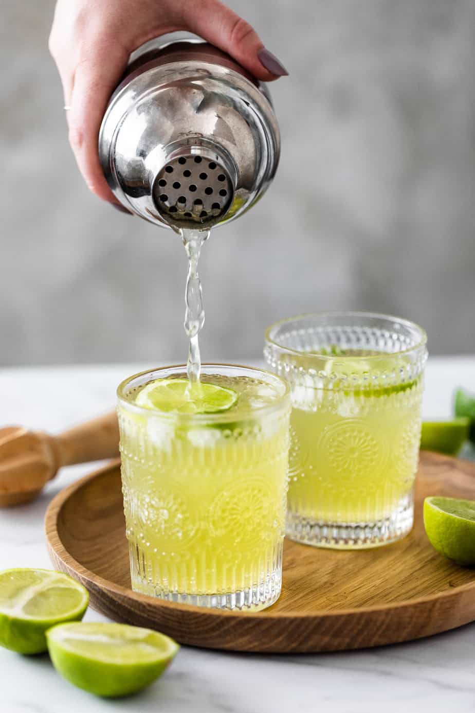 Two glasses of Tokyo tea sitting on a wooden tray surround by lime wedges.