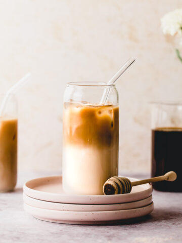 A tall glass of honey almond milk cold brew sitting on a small plate.