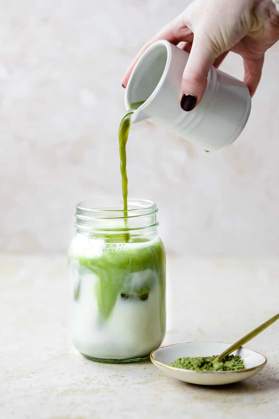 Matcha being poured into a mason jar full of ice and milk. 