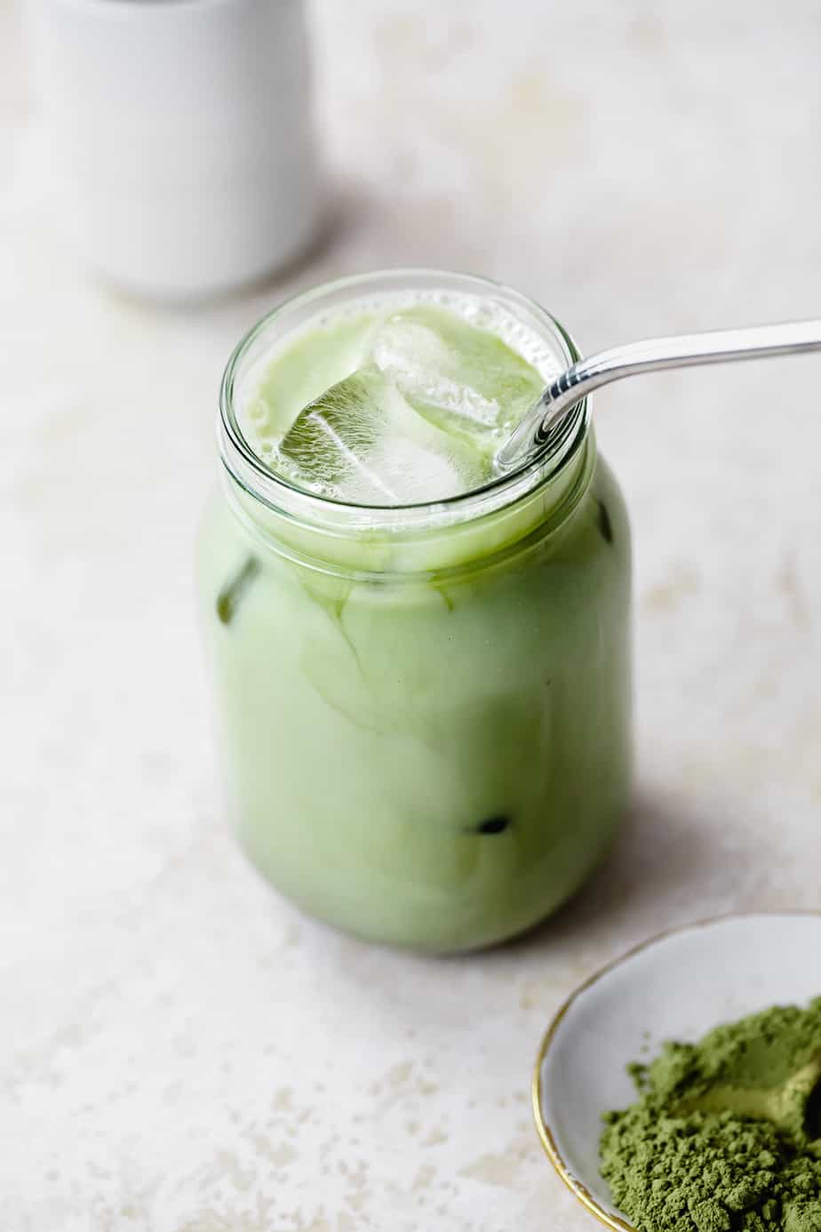 A mason jar filled with green tea matcha and milk sitting on a white table.