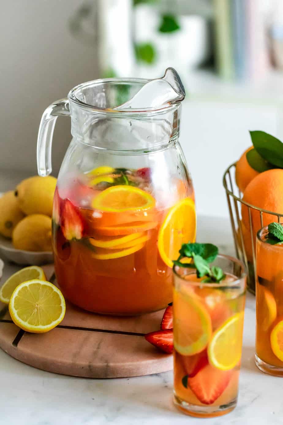 A large jug filled with iced peach green tea and slices of fresh fruit.