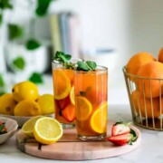 Two glasses of iced peach green tea lemonade sitting on a wooden tray with some lemon slices.